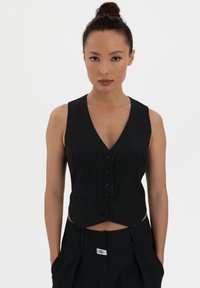 Black pinstripe vest with a deep V-neck, six buttons down the front, and a slightly cropped design. Smooth fabric, tailored fit.