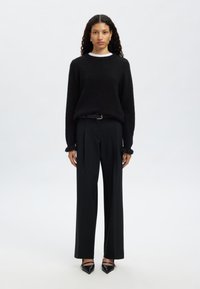 Svart stickad tröja med avslappnad passform och långa ärmar, kombinerad med högmidjade svarta byxor med bälte och eleganta svarta klackskor.