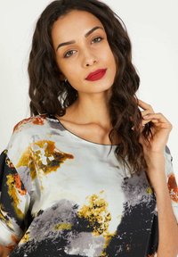 Blusa de satén con un corte suelto, que presenta un patrón abstracto multicolor en tonos de negro, naranja, gris y amarillo. Escote en forma de u.