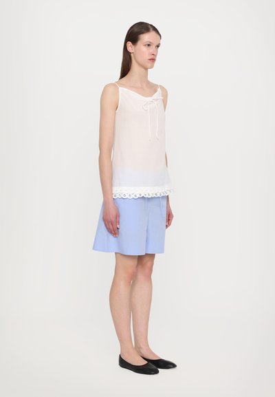 White sleeveless top with a bow detail and lace trim at the hem, paired with light blue striped shorts and black flats.