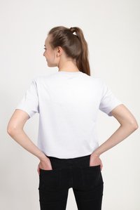 Bílé bavlněné tričko s klasickým kulatým výstřihem, krátkými rukávy a volným střihem, zobrazena zezadu na jednobarevném pozadí.