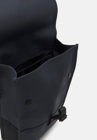 Kék vízálló hátizsák, tetején fedéllel, patent zárral és oldalsó csattal; tágas belső terével és fekete szövet bélésével rendelkezik.
