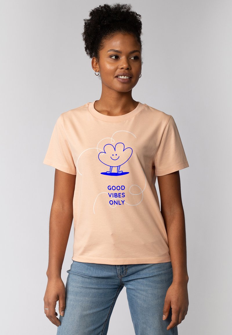 Perzikkleurig katoenen t-shirt met een blauwe grafische afbeelding van een lachende plant en de tekst "GOEDE VIBES ALLEEN" eronder, ronde halslijn, korte mouwen.