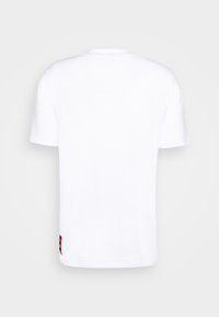 Biała bawełniana koszulka z krótkim rękawem, okrągłym dekoltem oraz małą czerwoną metką na dolnej lewej stronie. Gładka faktura i klasyczny krój.