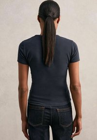 Tricou ajustat de culoare bleumarin închis, cu mâneci scurte și decolteu rotund, purtat cu blugi închiși. Material neted, siluetă elegantă, design minimalist.