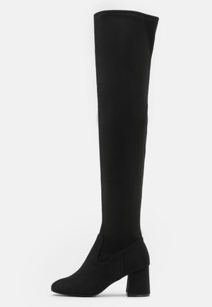 Botte noire femme cuissarde avec talon bloc et bout arrondi sur fond blanc.