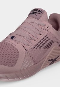 Κοντινό πλάνο αθλητικού παπουτσιού Reebok σε λιλά χρώμα με διχτυωτά πάνελ, κορδόνια και το λογότυπο της Reebok στη γλώσσα και τη μεσαία σόλα.