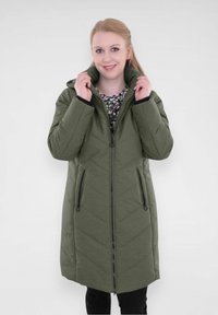 Manteau long en olive, rembourré, avec des coutures en chevron, fermeture zippée et poches latérales. Dispose d'un col montant et d'un tissu doux et texturé.
