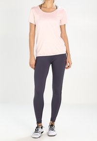 Camiseta de algodón rosa claro con escote redondeado, combinada con leggings gris oscuro. Zapatillas deportivas negras con suelas blancas. Textura de tela suave.