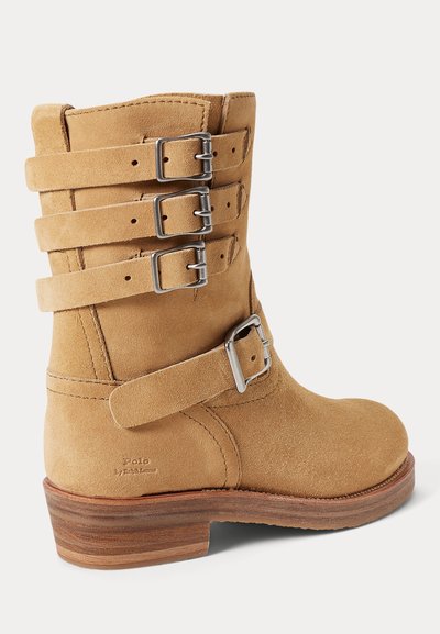 Semiš gležnjar v svetlo rjavi barvi s štirimi dekorativnimi trakovi in srebrnimi sponami. Zaobljeni prst in rjav slojevit petni podplat. Logotip blagovne znamke vrezan na strani.