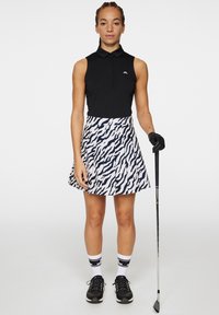 Svart ärmlös golfpolo, kjol med mönster i vitt och marinblått, svarta golfsko och svart handske. Kjolen har en utsvängd form med en vågig design.