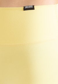 Gula högmidjade leggings i mjukt tyg, med slät yta och en synlig varumärkesetikett vid midjan.