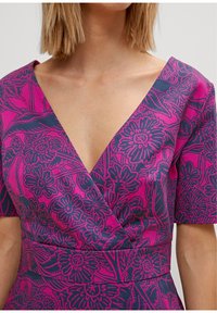 Abito fucsia con scollatura a V profonda, maniche corte, caratterizzato da un motivo floreale scuro. Il tessuto appare liscio con una silhouette aderente.