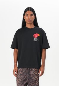 Sort bomulds T-shirt med korte ærmer, rund halsudskæring og et farverigt basketball-tema grafisk tryk på brystet. Stylet med prikkede bukser.