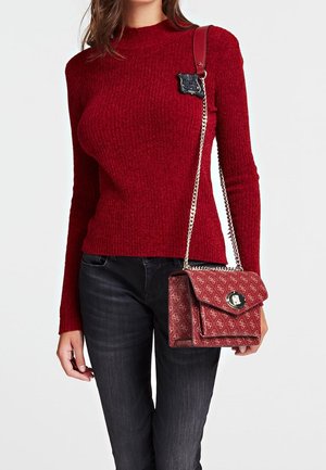 Pull rouge côtelé avec un col montant, associé à un sac à main maroon à motifs, doté d'une bandoulière en chaîne et d'un fermoir distinctif.