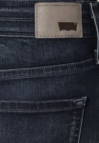 Mörkblå denimjeans med en grå läderlapp med logotyp, synlig sömnad och en klassisk femfickdesign.