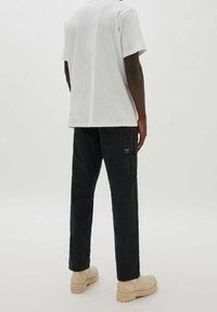Camiseta de algodón gris combinada con pantalones cargo negros. Los pantalones tienen bolsillos laterales y un parche, complementados con calzado beige de suela gruesa.