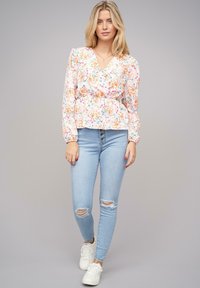 Blusa floreale con scollo a V, maniche lunghe a sbuffo e vita arricciata. Abbinata a skinny jeans strappati azzurri chiari e sneakers bianche.