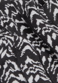 Tissu tricoté noir et blanc avec un motif géométrique, présentant des designs en zigzag et ondulés. Texture douce avec une épaisseur de fil variée.
