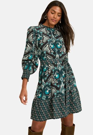 Floral patterned dress featuring puff sleeves, a gathered waist, and a flared skirt. Main colors are teal, black, and cream. Textured fabric.