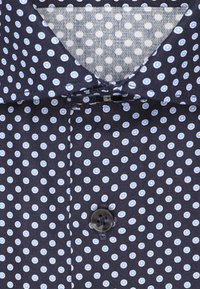 Camicia blu navy con pois circolari bianchi e azzurri, dotata di un singolo bottone nero fissato e un colletto pieghevole con un rivestimento interno a pois grigi chiari.