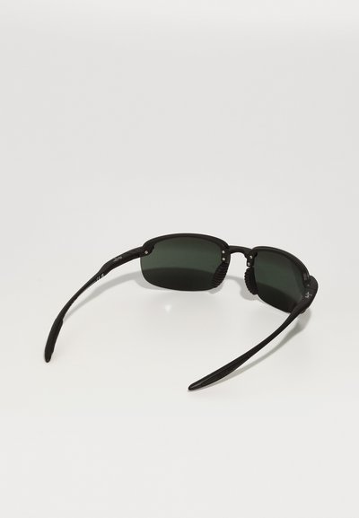Black sunglasses with green lenses, featuring a sleek design, curved black arms, and textured accents on the temples for grip.