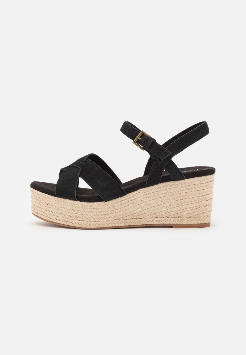 Sandale compensée en suède noir avec brides croisées, boucle à la cheville et semelle plateforme en fibres naturelles tissées.