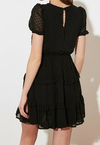 Vestido negro con capas en capas, mangas cortas abullonadas y un corte en forma de ojo de cerradura en la espalda. Fabricado con un tejido ligero y texturizado con un patrón de puntos.