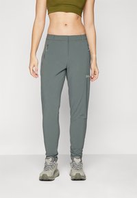 Graue, tapered Wanderhose mit Reißverschlusstaschen, aus leichtem Material gefertigt. Getragen mit grauen Wanderschuhen, die über strukturierte Sohlen verfügen.