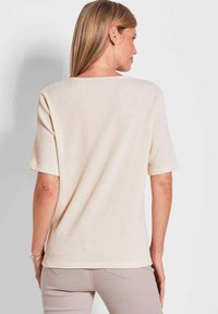 Korte mouwen, textuur lichtbeige top met een ronde hals en rechte snit, voorzien van een subtiel geribbeld patroon en een relaxte pasvorm.