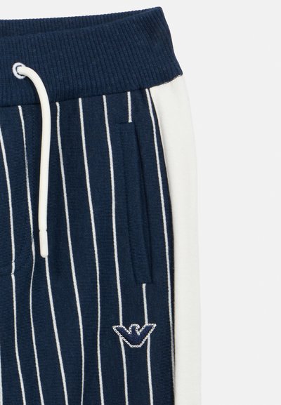 Μπλε ναυτικό ριγωτό παντελόνι φόρμας με ριμπ ζώνη μέσης, λευκές πλαϊνές λωρίδες, μπροστινές τσέπες και κεντημέ νο λογότυπο στην αριστερή πλευρά.