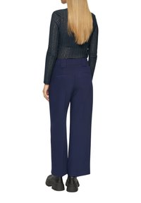 Marineblauwe wijde broek met een gladde textuur en achterzakken, gecombineerd met een fitted, geribbelde, lang mouwtop in donker marineblauw met verticale strepen.