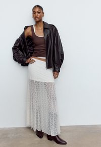 Sort læder oversize jakke, brun tanktop, gennemsigtig hvid blonde maxi nederdel og brune ankelstøvler med spidse tæer. Markant ringdetalje.