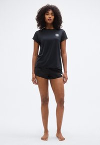 Μαύρο αθλητικό μπλουζάκι με κοντά μανίκια και στρογγυλή λαιμόκοψη, συνδυασμένο με μαύρο σορτς. Και τα δύο κομμάτια είναι απλά και κατασκευασμένα από ελαφρύ ύφασμα.