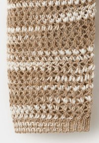 Gros plan d’un tissu tricoté beige et blanc avec une texture ouverte et aérienne et un motif de rayures alternées.