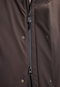 Bruine windjack met een voorrits, zwart beslag, drukknoopsluitingen en een gladde textuur met een subtiele glans.