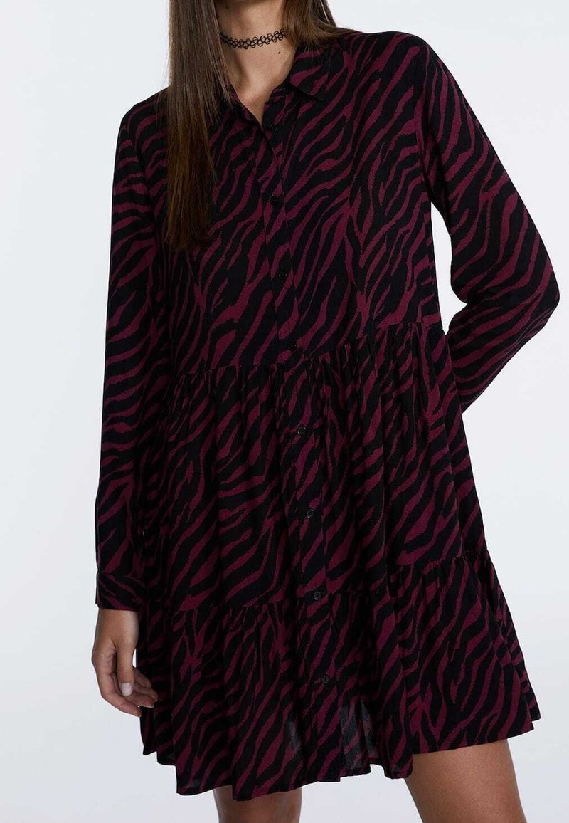 Schwarz-lila gestreiftes Kleid mit durchgehender Knopfleiste, langen Ärmeln und gestuftem Rockdesign. Weicher Stoff mit ausgeprägtem Tiermuster.