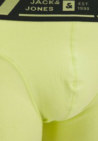 Limoengroene herenenonderbroek met een zwarte elastische tailleband en witte tekst. De stof is glad met minimale naden voor comfort.