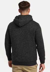 Sweter z kapturem dziergany w ciemnoszarym kolorze, z teksturowanym wzorem, ściągaczami przy rękawach i dolnym brzegu oraz podszewką w kapturze. Widok z tyłu.