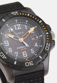 Timex Expedition solar sat ima crni teksturirani brojčanik, odvažne bijele i narančaste oznake, te izdržljivu crnu platnenu narukvicu. WR 50M.