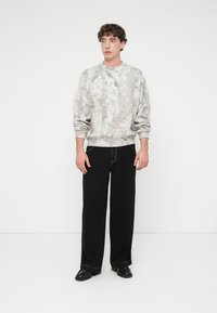 Ανοιχτό γκρι φούτερ με υφή εμπνευσμένη από τη φύση, σε συνδυασμό με μαύρο παντελόνι φαρδιάς γραμμής. Μαύρα παπούτσια ολοκληρώνουν την εμφάνιση.