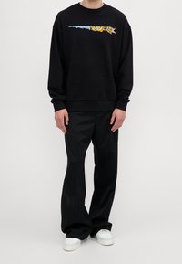 Felpa nera con una grafica colorata sul petto, abbinata a pantaloni neri e sneakers bianche. Tessuto morbido, vestibilità comoda.