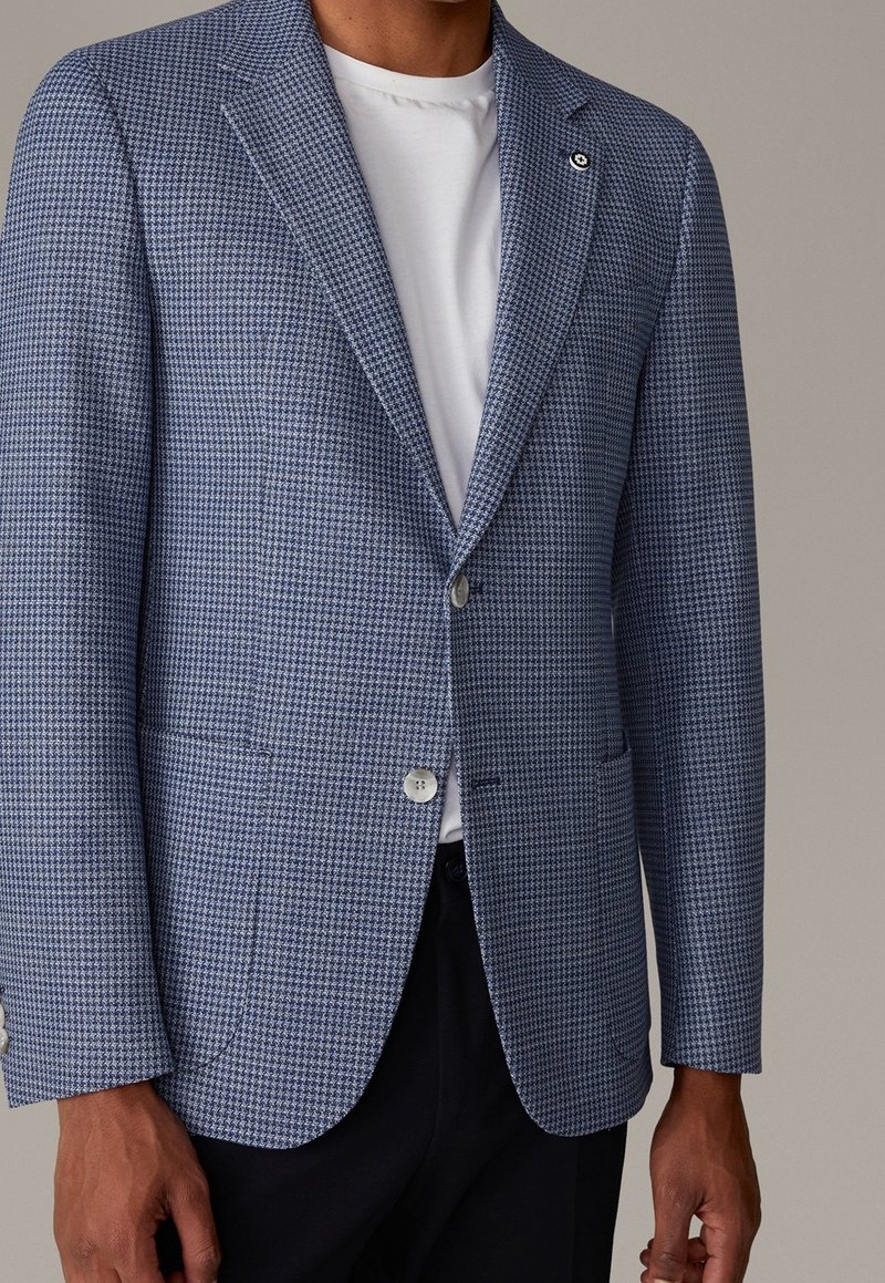 Jasnoniebieska marynarka w pepitkę z klapami z wycięciem, dwoma przednimi kieszeniami i srebrnymi guzikami, zestawiona z białym t-shirtem z okrągłym dekoltem pod spodem.