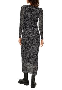 Langärmliges schwarzes Kleid mit einem floralen weißen Muster, aus transparentem Material. Es hat eine körperbetonte Silhouette und einen mittellangen Saum. Schwarze Stiefel sind zu sehen.