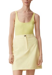 Gelbes, geripptes Tanktop kombiniert mit einem hellgelben A-Linien-Rock, der einen Frontknopf und einen ordentlich gefalteten Saum hat.