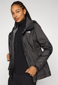 Čierna vodotesná bunda s kapucňou, so zipsovým a suchým zipsom na uzatváranie, nastaviteľnými manžetami a logom North Face na hrudi.