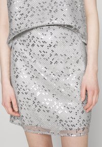 Robe mini en sequins argentés avec un motif géométrique. Elle présente un haut à coupe ample et une jupe ajustée, ornée de sequins réfléchissants sur toute la surface.