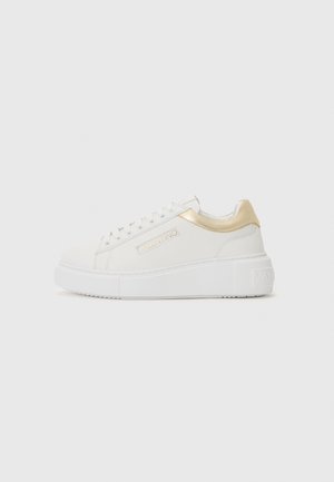 Sneakers bianchi con tomaia testurizzata, dettagli dorati sul tallone e ai lati, e una robusta suola platform bianca. Logo visibile di lato.