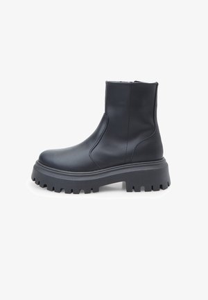 Cizmă până la gleznă, de culoare neagră, fabricată din piele netedă, cu o talpă groasă cu finisaj texturat și fermoar pe lateral pentru a fi ușor de purtat.