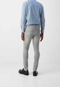 Přiléhavé šedé džíny z denimu s vybledlým efektem, designem s pěti kapsami a jemnými švy, doplněné světle modrou kostkovanou košilí a černými botami.